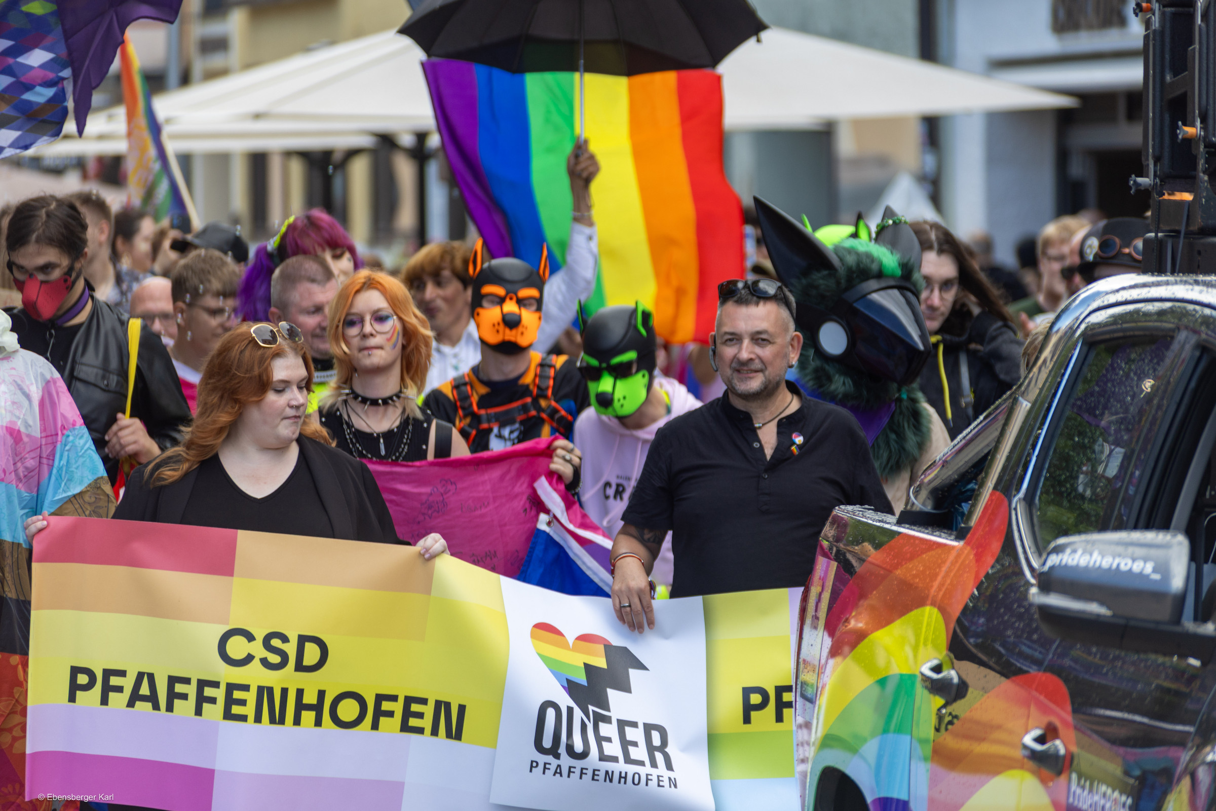 Die CSD-Parade mit Vereinsbanner und großer Regenbogenflagge zieht durch Pfaffenhofen.