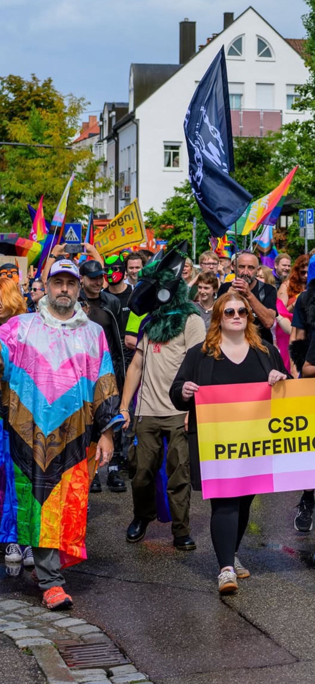 Teilnehmende in farbenfroher Kleidung tragen Banner und Fahnen während der CSD-Parade.