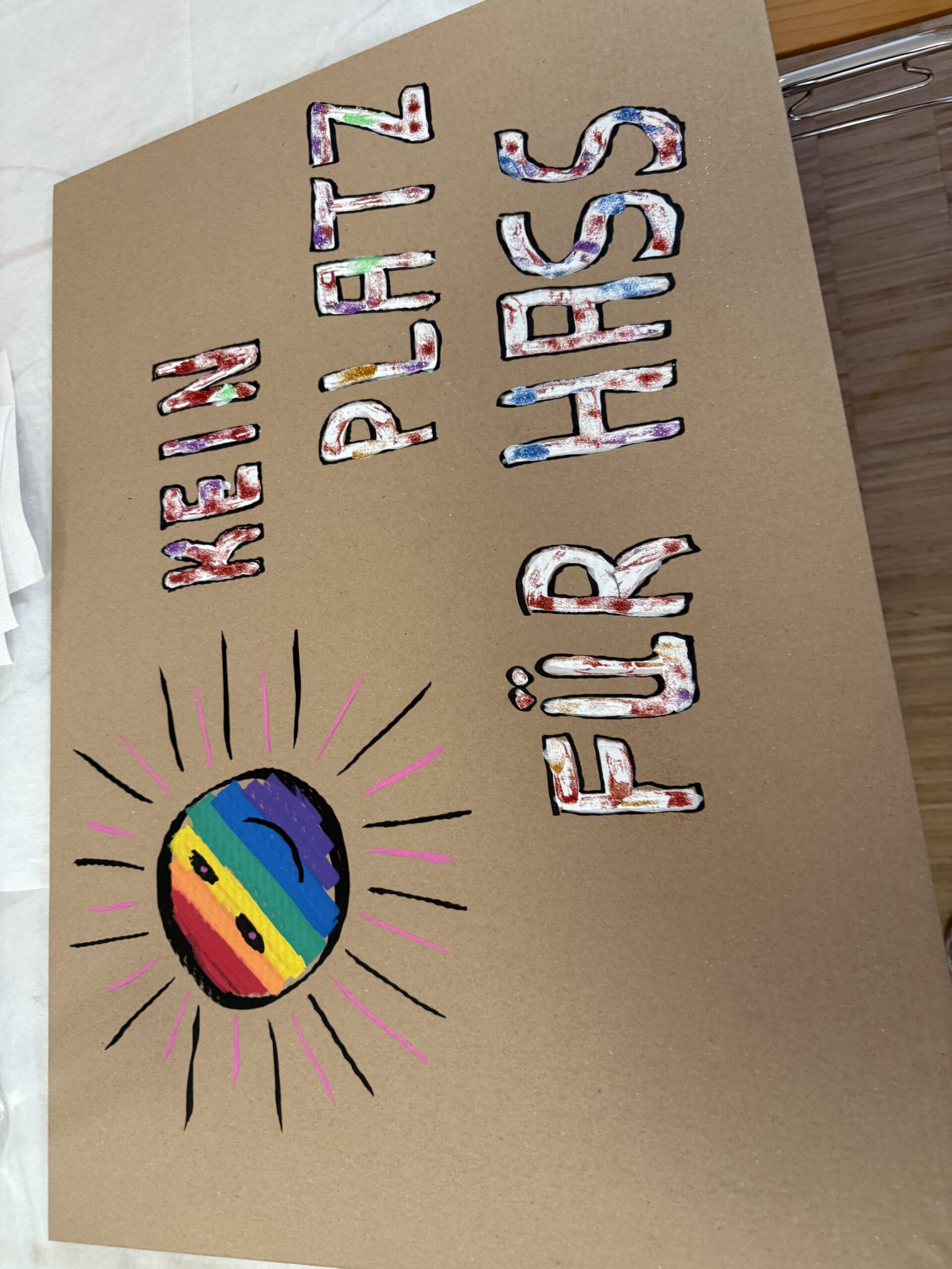 Handgemaltes Pappschild mit Regenbogensonne und der Aufschrift „Kein Platz für Hass“.