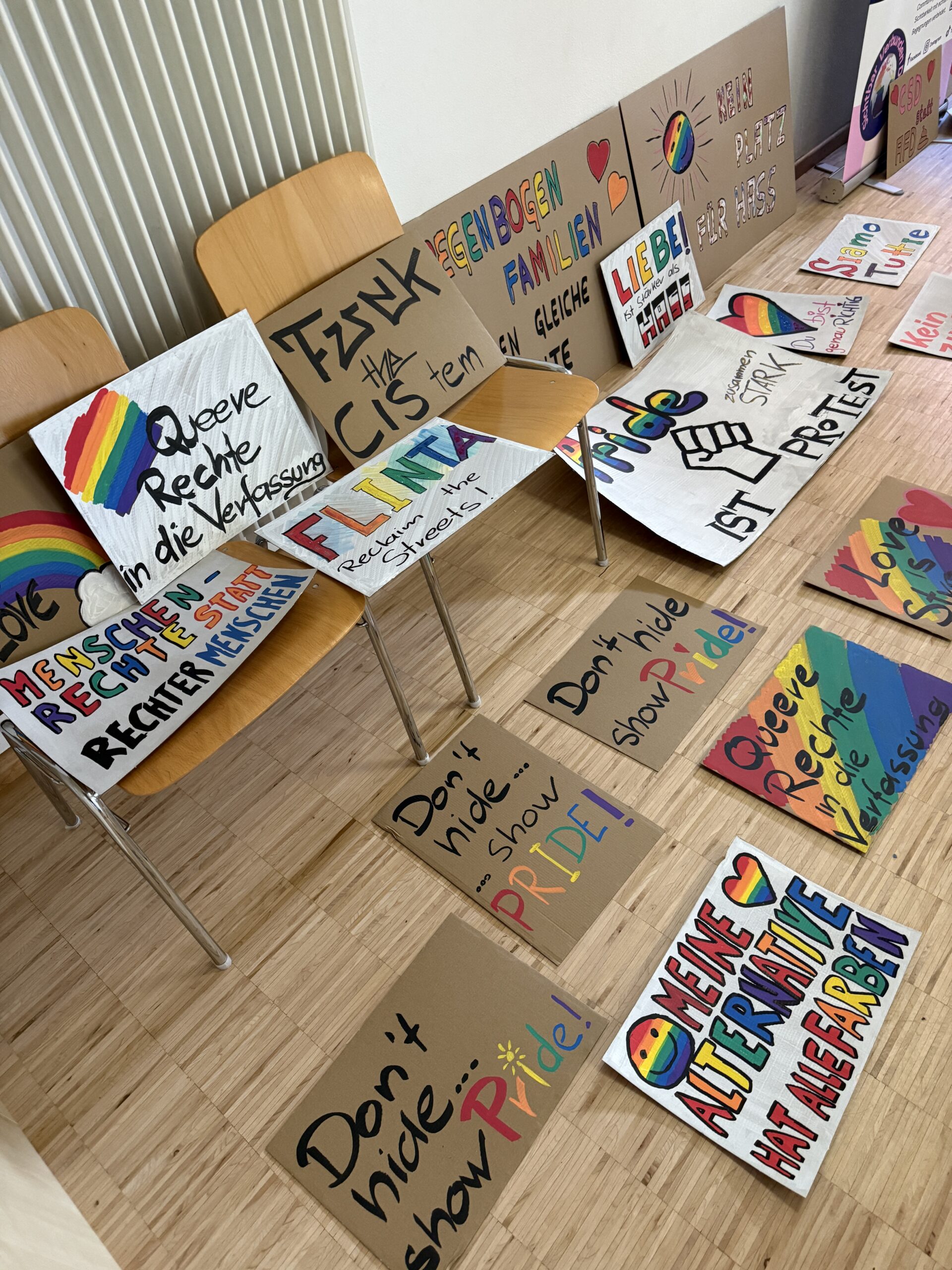 Mehrere selbst gestaltete Plakate mit bunten Schriftzügen und Regenbogenmotiven liegen im Pfarrsaal aus.
