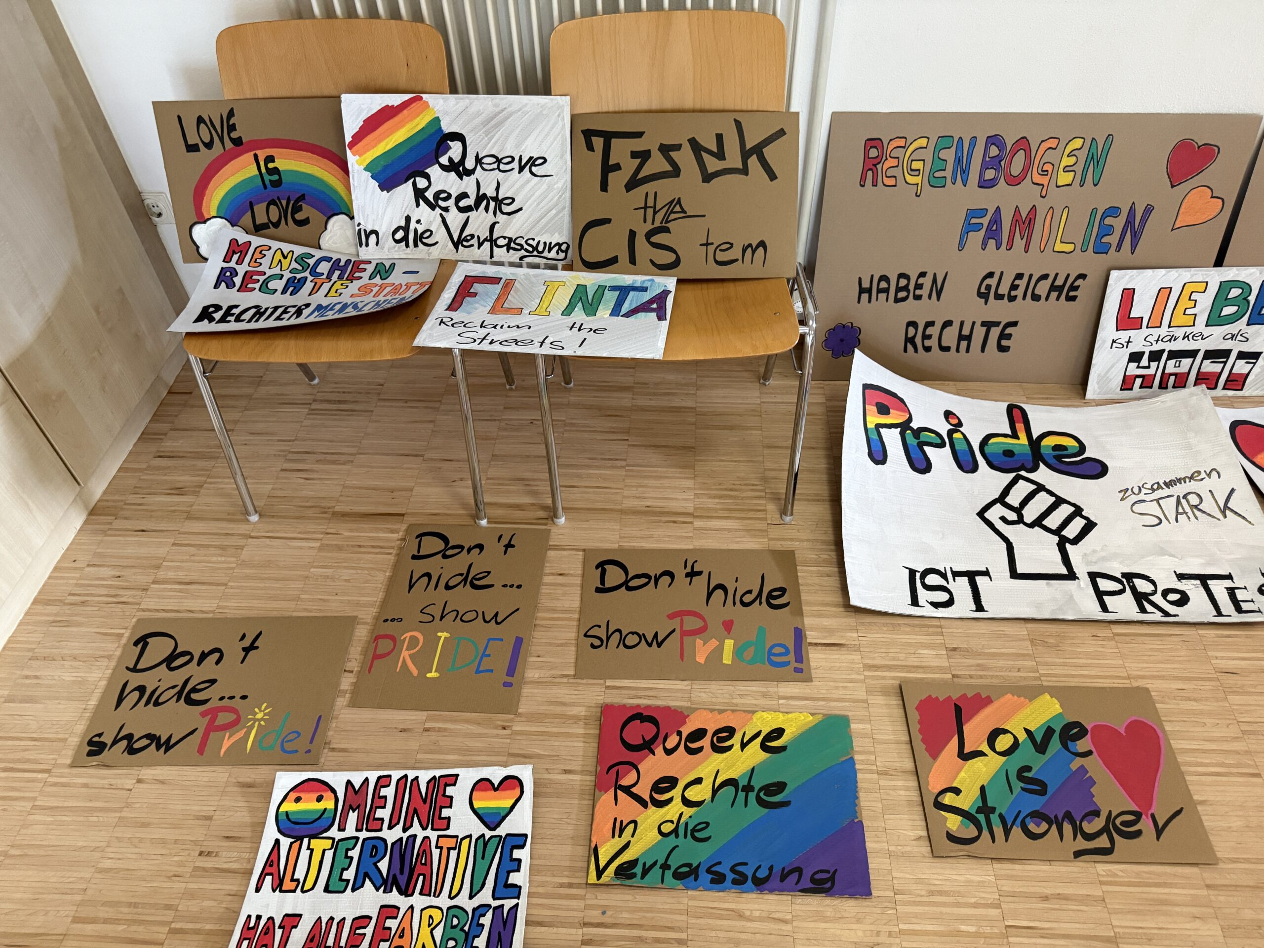 Fertige Demonstrationsplakate mit Regenbogenfarben und Schriftzügen stehen an Stühlen und liegen auf dem Boden.