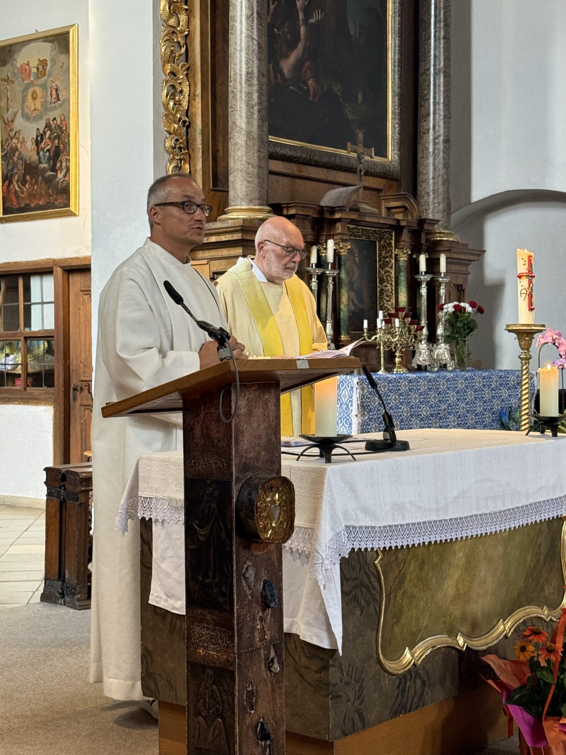 Mitwirkende der Queeren Andacht stehen am Lesepult vor dem Altar und der Regenbogendekoration.