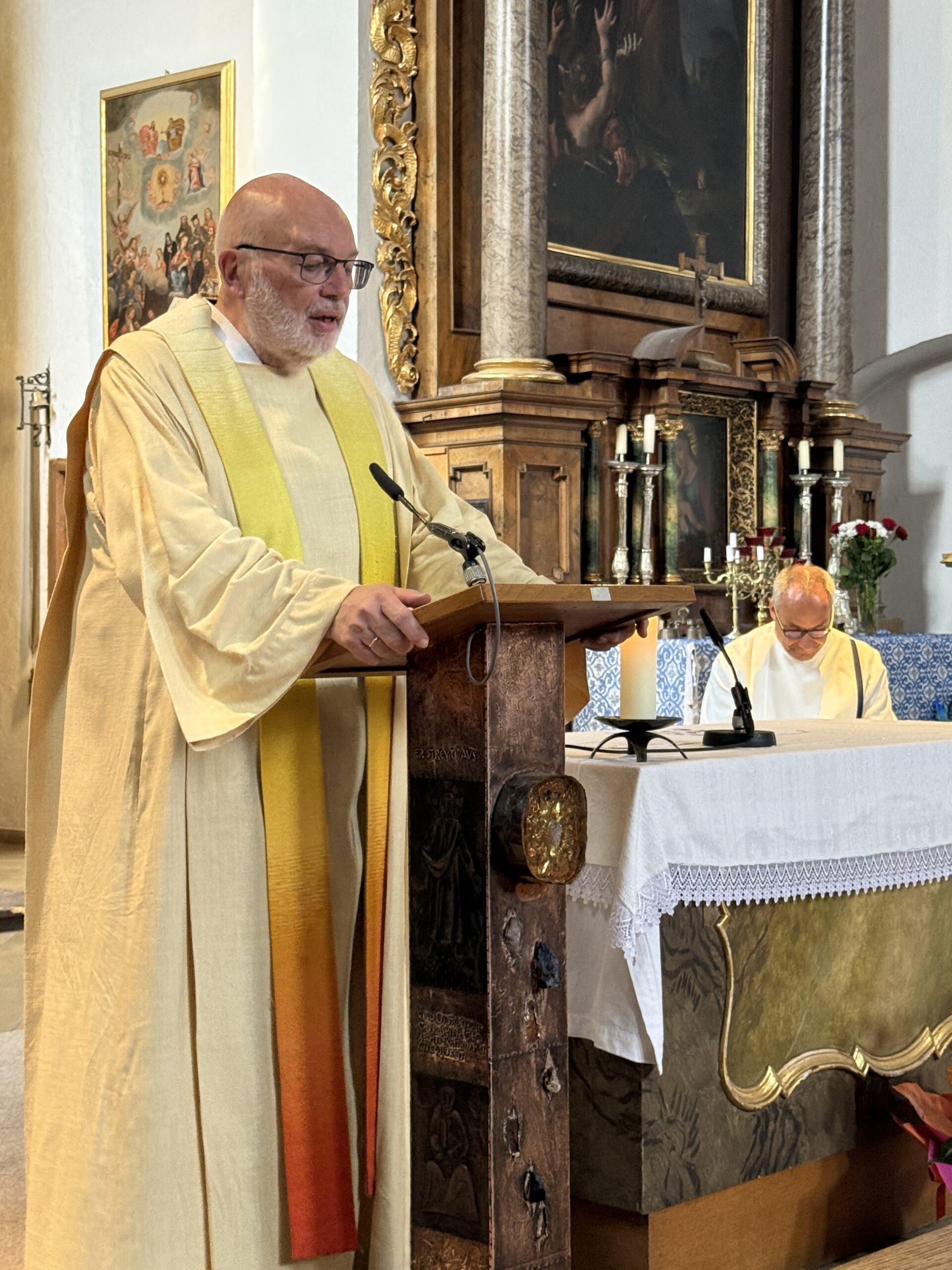 Eine Person in hellem Gewand spricht am Lesepult vor dem Altar.