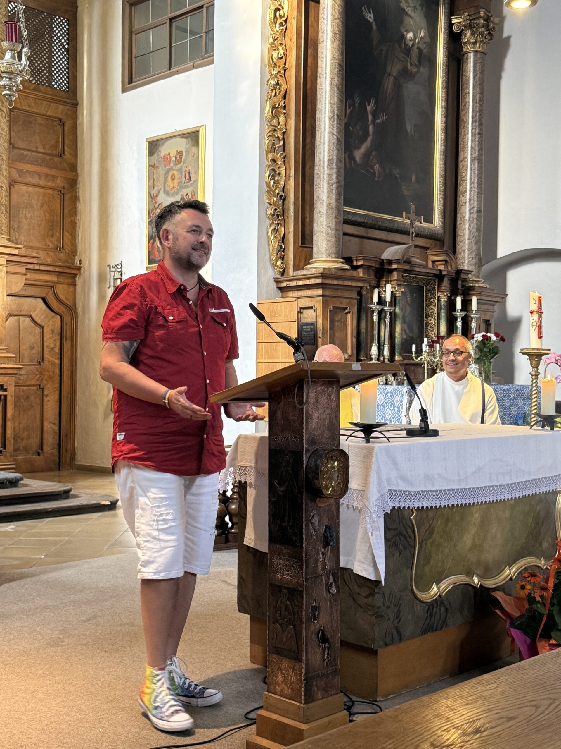 Eine Person im roten Oberteil spricht bei der Queeren Andacht am Lesepult im Kirchenraum.