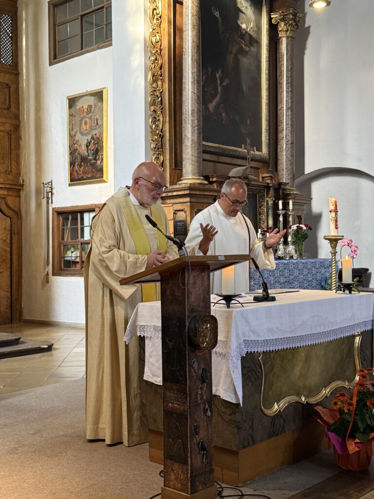 Zwei Mitwirkende am Lesepult vor dem mit Regenbogenfarben geschmückten Altar bei der Queeren Andacht.